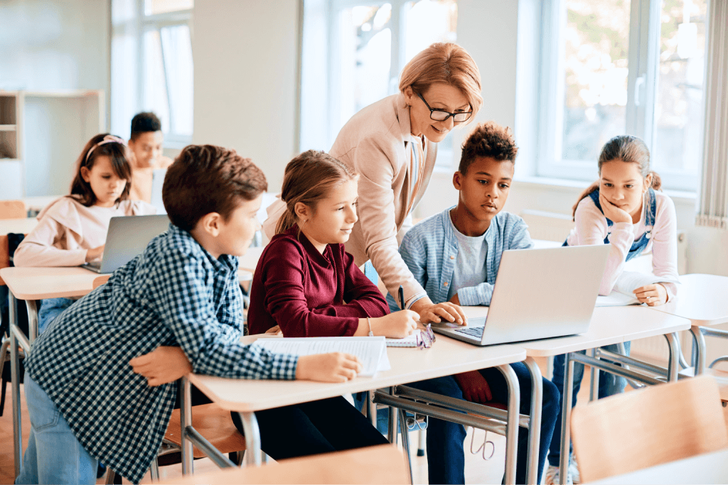 Teacher helping a group of school pupils with their work at a classroom desk