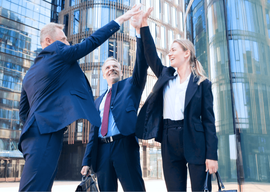 Three colleagues celebrating with a high-five outside a glass office